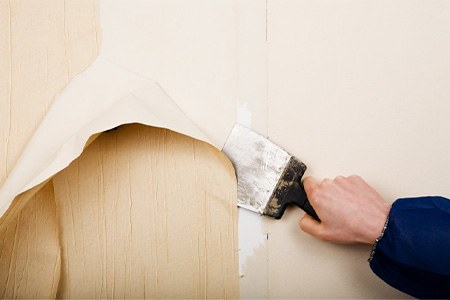 A contractor removing wallpaper from the wall