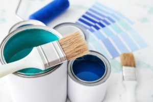 different paint swatches of blue laying on a counter with two paintbrushes and two cans of blue paint