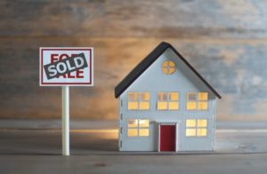 a small model home with a "for sale" sign in front of it and a "sold" sticker placed over the sign